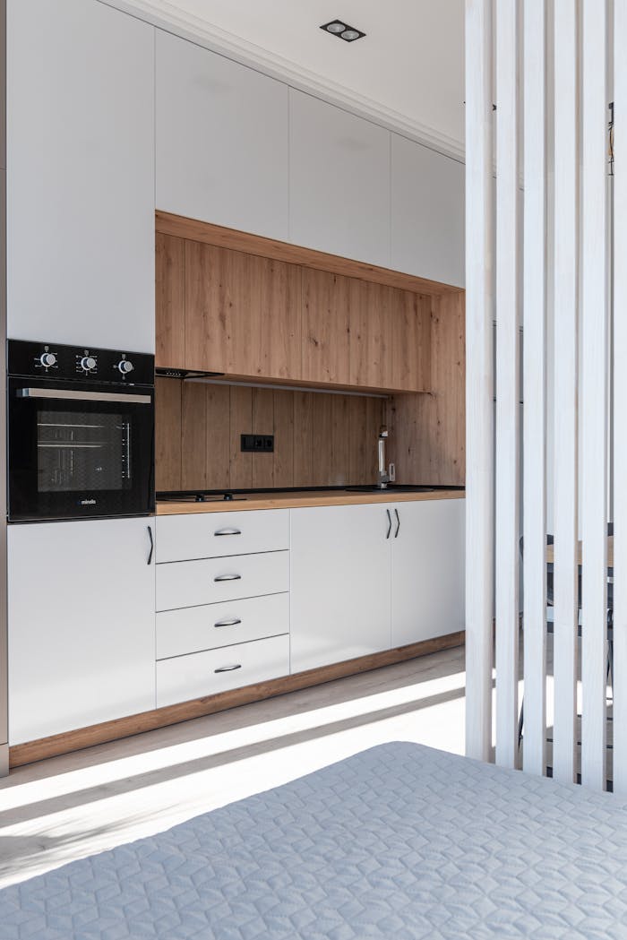 Interior of bright modern room with open kitchen with cupboards and oven next to bed